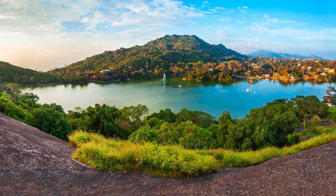 Panoramic view of Nakki Lake surrounded by lush green hills and Mount Abu town under a clear blue sky – JKV Travel.